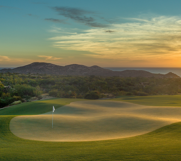 Twin Dolphin Los Cabos Golf Course image at sunset overlooking the mountains and ocean.